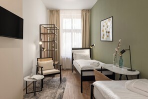 A modern bedroom with a bed, a chair, a small table, a bedside table, a TV, and a window with curtains. - Youngmann House (Prague)