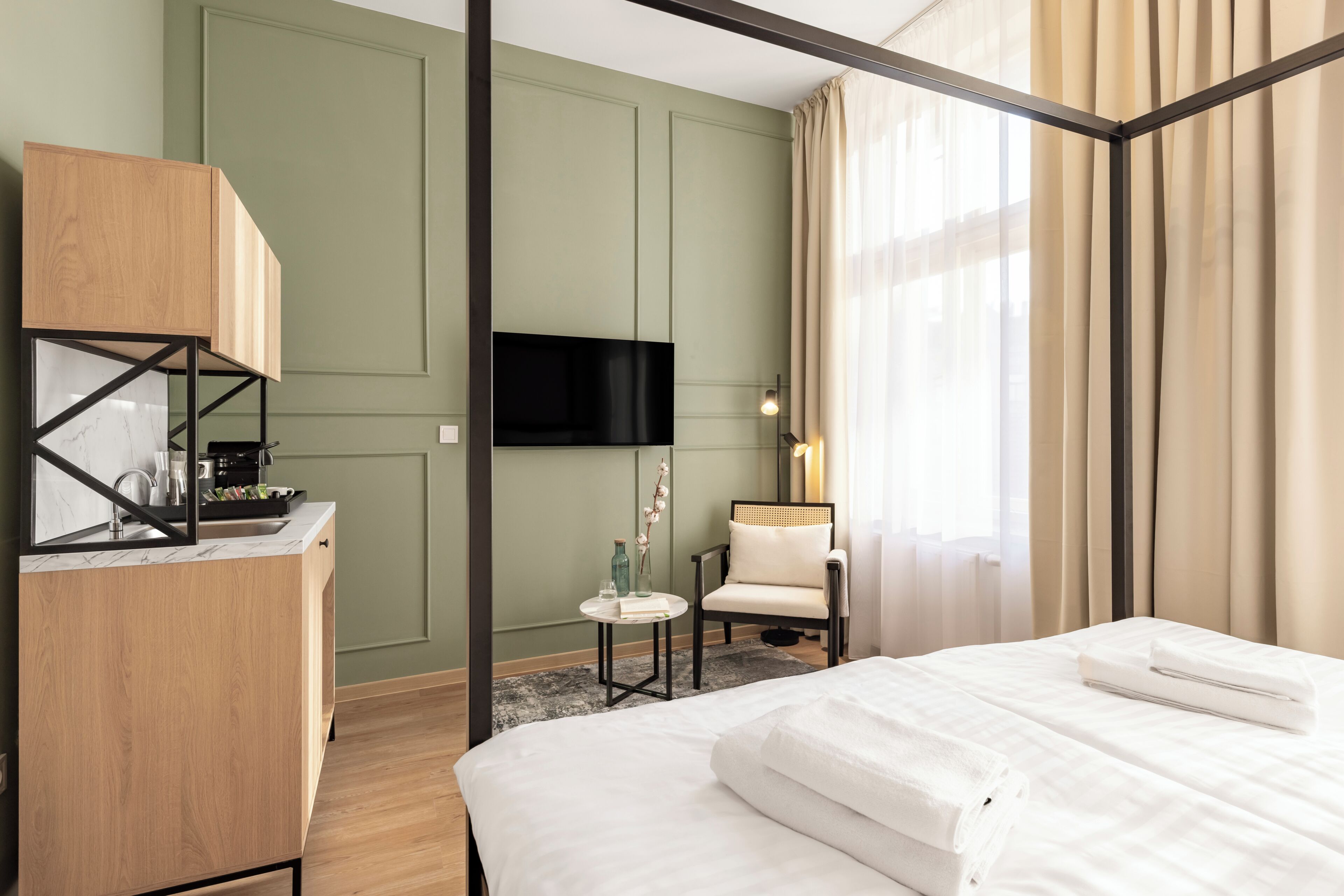 Habitación de hotel con cama, escritorio con televisor de pantalla plana, una silla y una mesita de noche con lámpara.