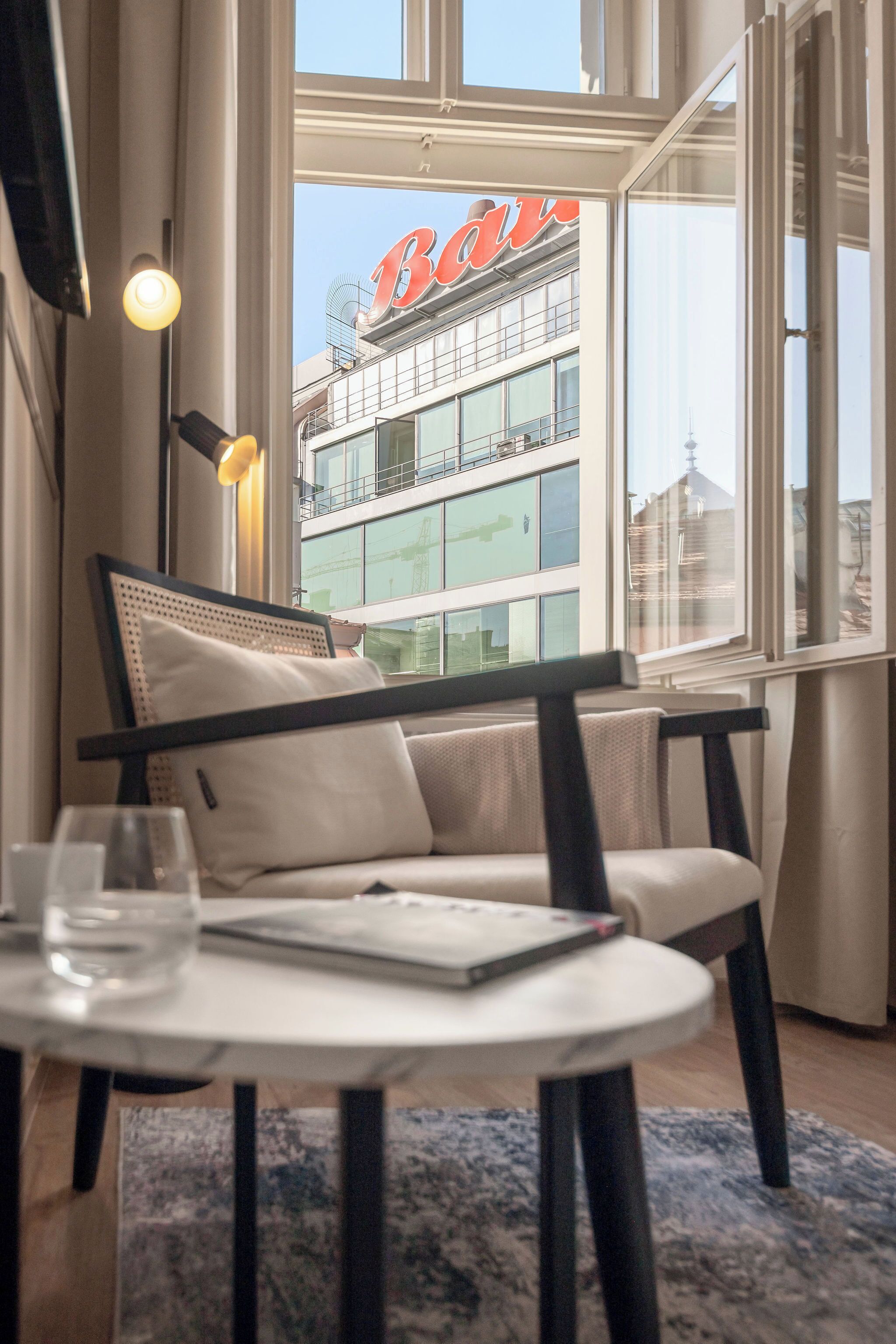 A modern interior with a sofa, a table with a glass, and a view of a building with a red sign.
