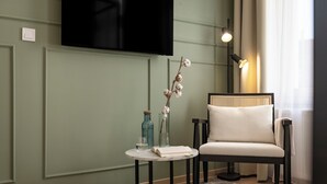 A modern living room with a flat-screen TV mounted on the wall, a round side table with a book and a glass, a chair with a woven backrest, and a floor lamp. - Youngmann House (Prague)