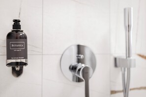 A bathroom with a wall-mounted bottle of Botanica with Argan Oil hair and body shampoo, a modern showerhead, and a chrome faucet. - Youngmann House (Prague)