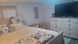 A bedroom with a bed, a dresser, a television, and a small table. - Nice 1-bedroom cottage with AC in charming West Liberty (West Liberty)
