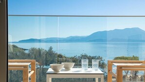 Un balcón con mesa y sillas, con vista a una masa de agua y montañas a lo lejos.