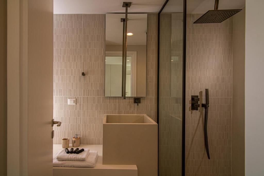 Een moderne badkamer met een douchecabine van glas, een beige wastafel en een spiegel boven de wastafel.