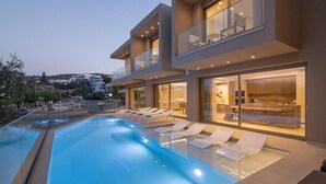 Una casa moderna de dos pisos con piscina, sillas de tomar el sol y vistas del entorno.