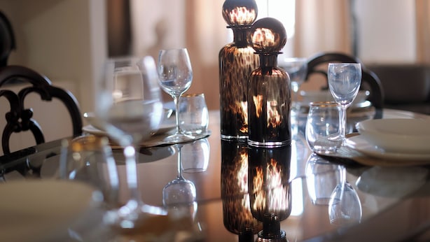 A dining table with a reflective surface, two glass decanters, and several empty wine glasses. - Ponte Vecchio SPA & Lift (Firenze)