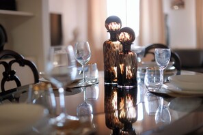 Una mesa de comedor con superficie reflectante, dos jarrones de cristal y varios vasos de vino vacíos.
