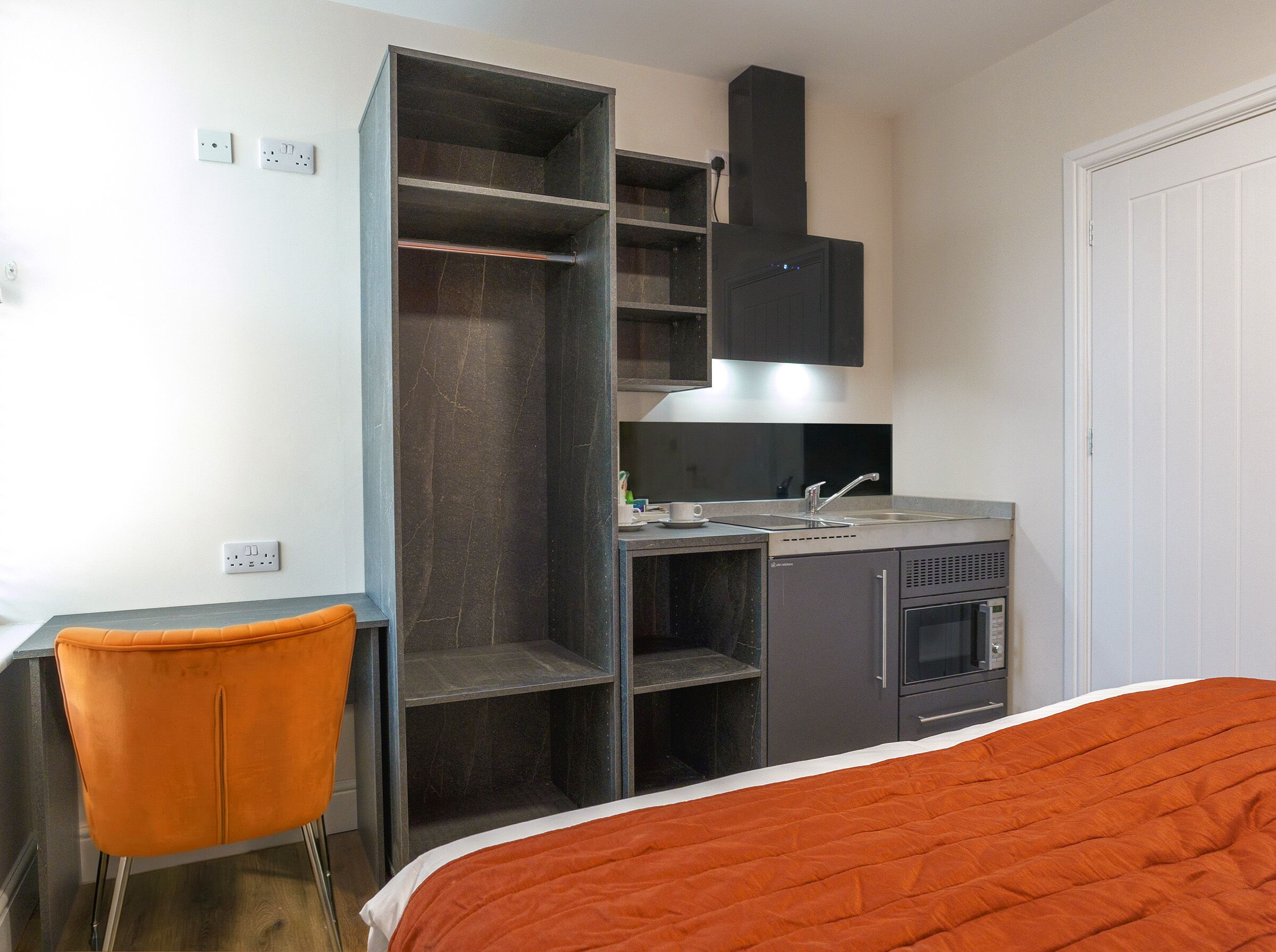 Une chambre d’hôtel de taille réduite, comprenant un lit, un bureau, une kitchenette et une armoire.
