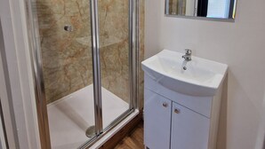 Ένα μπάνιο με ένα ντους που διαχωρίζεται με γυάλινο διάφραγμα, έναν λευκό νιπτήρα και έναν καθρέφτη ακριβώς από πάνω.