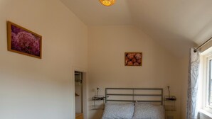Une chambre à coucher comprenant un lit, des tables de chevet, un luminaire au plafond, une fenêtre avec des rideaux et deux tableaux encadrés accrochés au mur.