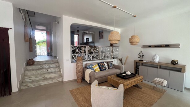 En moderne stue med sofa, sofabord og dekorative genstande. En trappe fører op til et andet rum.