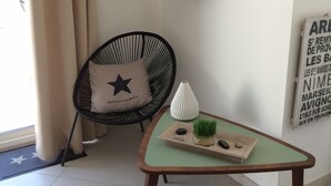A room with a round mirror on the wall, a black chair with a star pillow, and a small table with a plant and decorative items. - Appartement proche du centre historique, terrasse, clim et garage privé fermé. (Arles)