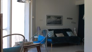A living room with a sofa, two chairs, a table, and a hanging light fixture. - Appartement proche du centre historique, terrasse, clim et garage privé fermé. (Arles)