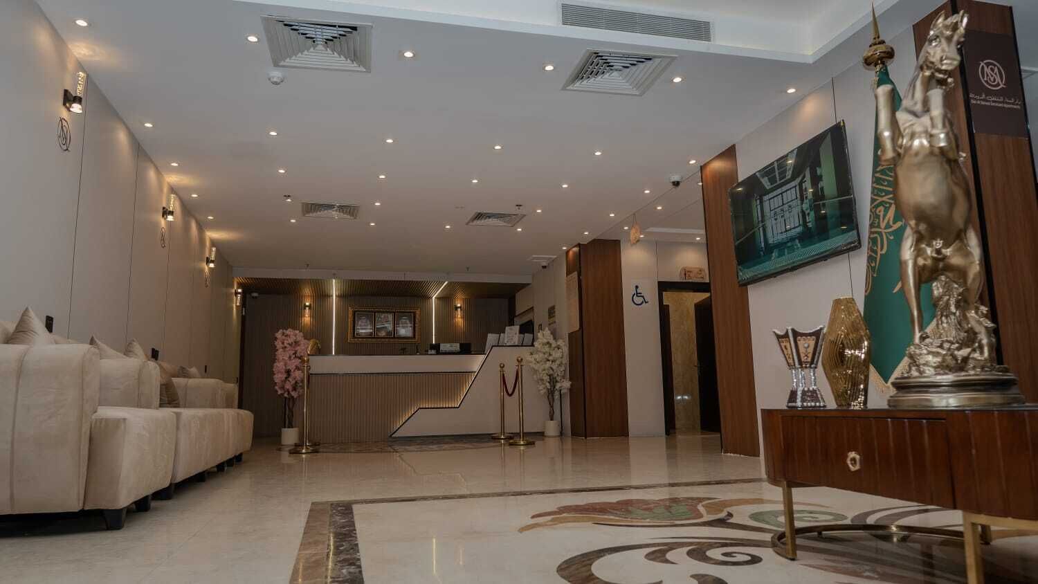 A hotel lobby with a reception desk, sofas, a staircase, and a statue.
