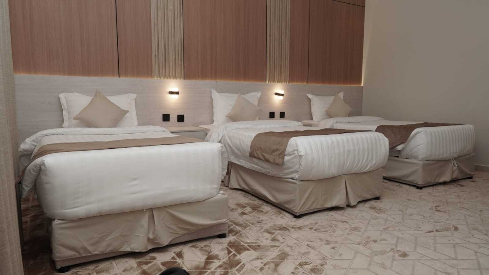 A hotel room with three beds, each with a headboard and bedside lamps.