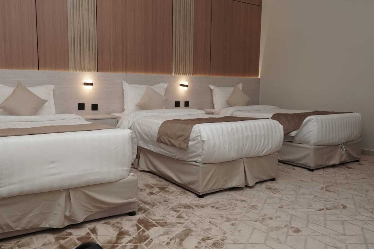 A hotel room with three beds, each with a headboard and bedside lamps.