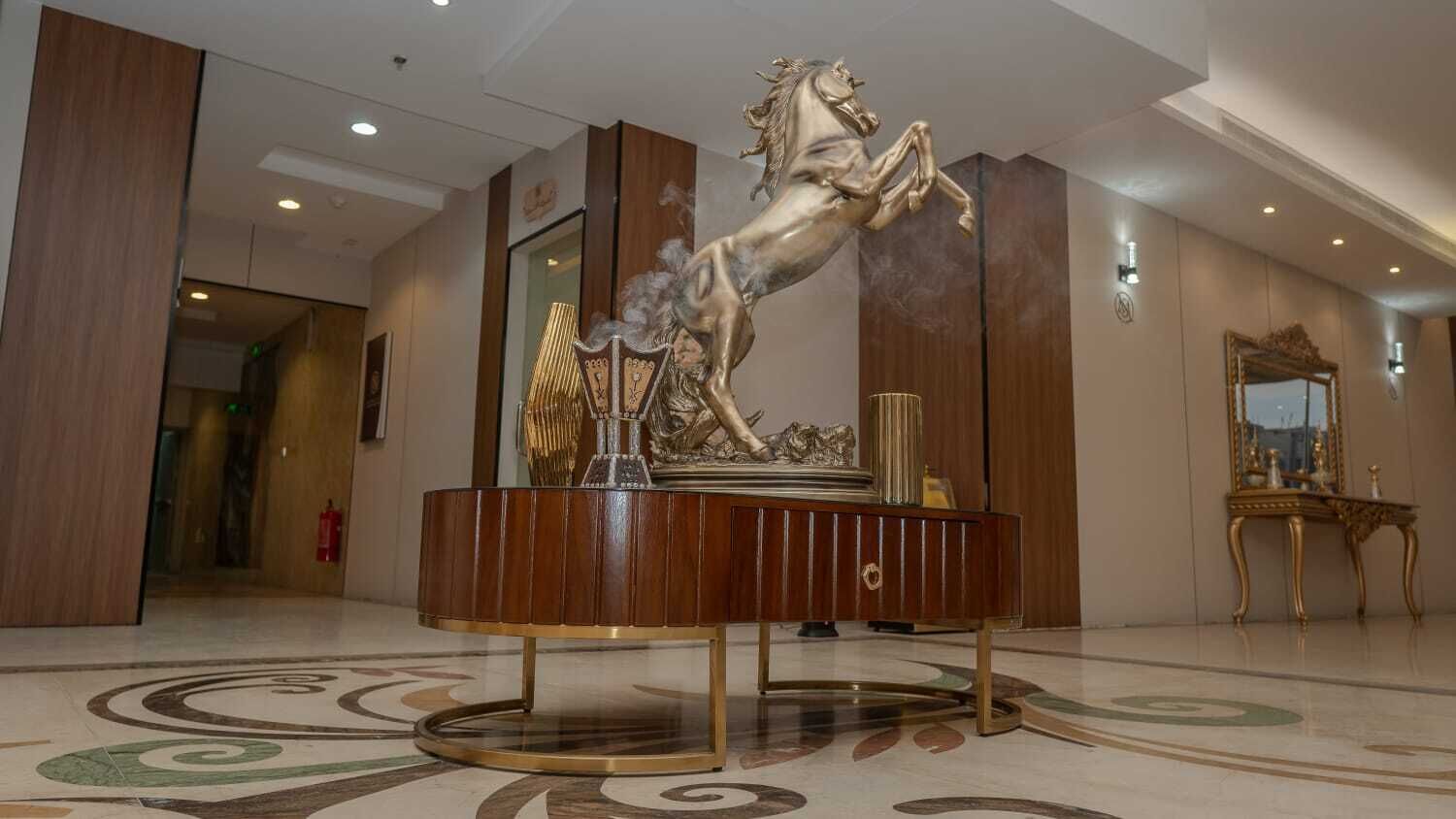 Eine Lobby mit einem runden Tisch in der Mitte, der eine goldene Skulptur eines Pferdes, einen Spiegel und eine dekorative Lampe zeigt.