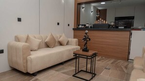 A modern living room with a beige sofa, a small wooden coffee table, and a kitchen area in the background.