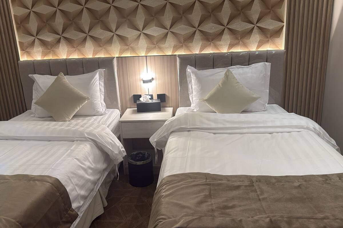 Een hotelkamer met twee bedden, een nachtkastje en een hoofdeinde met een geometrisch patroon.