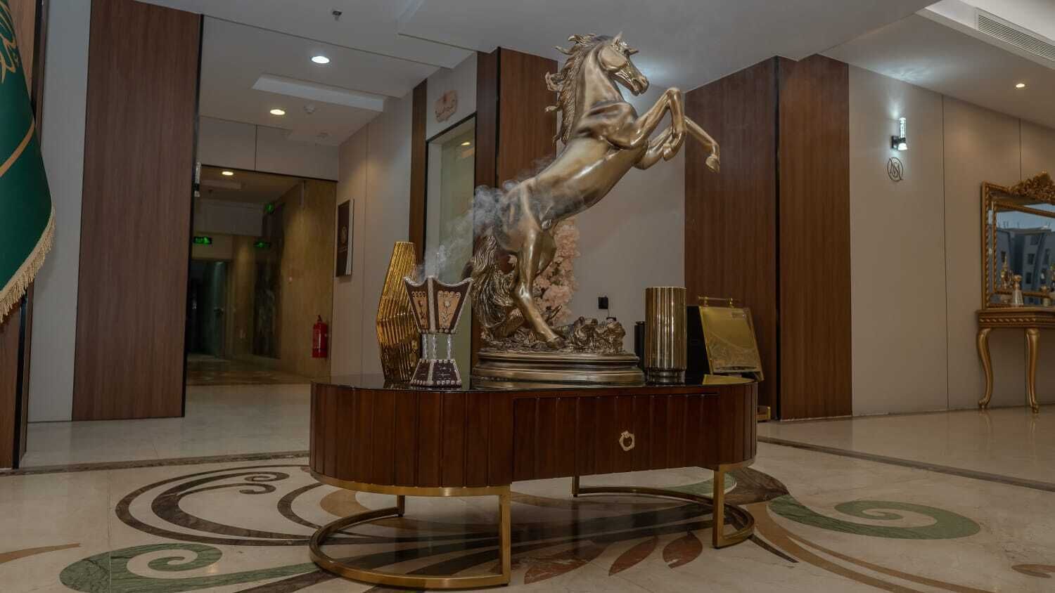 A lobby with a central round wooden console table featuring a horse statue, a mirror, and decorative items.