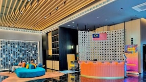 Un hall d’entrée moderne avec un canapé bleu, un comptoir d’accueil et un mur décoratif orné d’un drapeau malaisien.