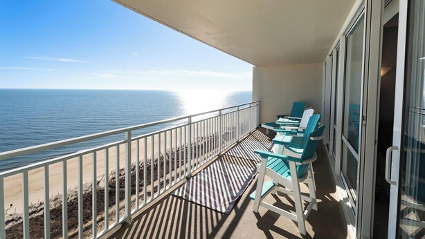 A balcony with a view of the ocean, featuring a railing, a table with chairs, and a glass door. - Oceanfront Carousel Condo • Beach Access Resort (Ocean City)