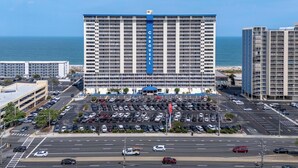 A high-rise hotel with a central blue stripe, a parking lot, and a view of the ocean. - Oceanfront Carousel Condo • Beach Access Resort (Ocean City)