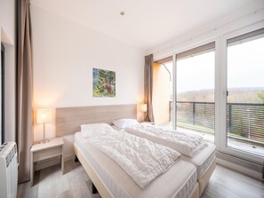 Et hotelværelse med en stor seng, et natbord med lampe, et billede på væggen og en balkon med udsigt.