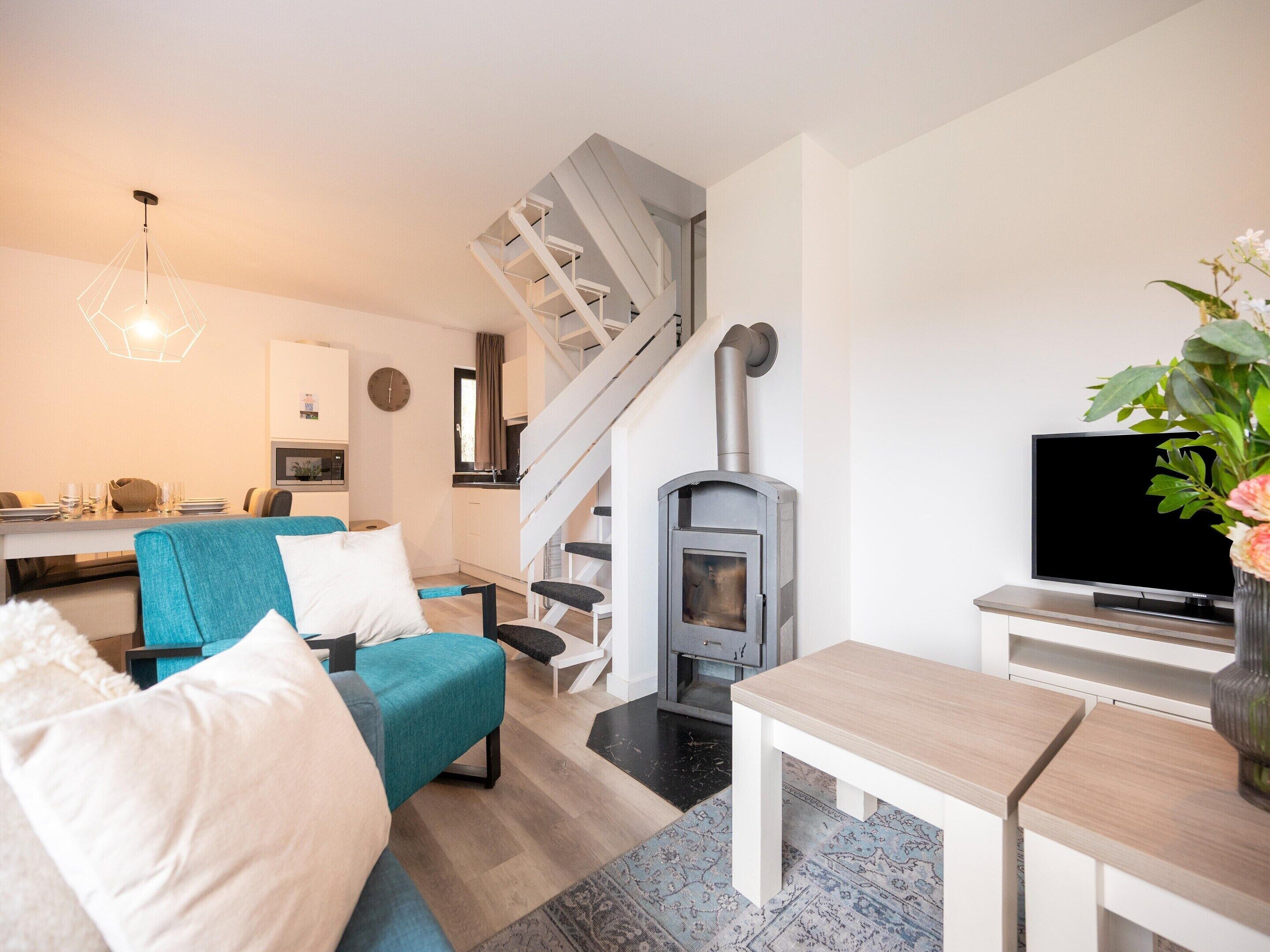 A modern living room with a staircase, a fireplace, a dining area, and a TV.