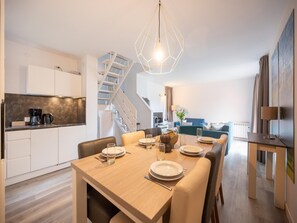 Et moderne køkken med hvide skabe, et spiseområde med et træbord dækket til fire personer, og en trappe, der fører op til en etage.