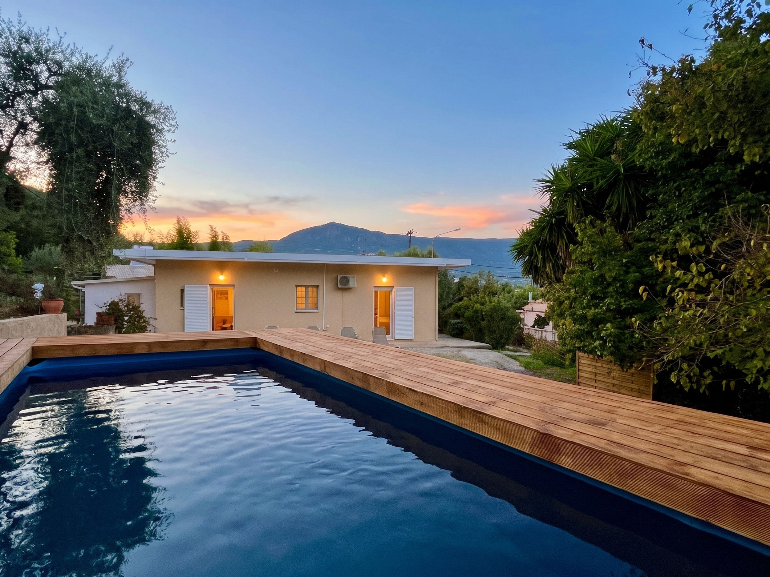 A modern house with a swimming pool, wooden deck, and a view of the sea and mountains.