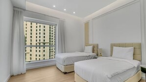 A hotel room with two beds, a large window with curtains, a wooden floor, and a view of buildings outside. - Sadaf 2701 (Dubai)