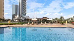 A swimming pool with lounge chairs and umbrellas, surrounded by buildings and palm trees. - Sadaf 2701 (Dubai)