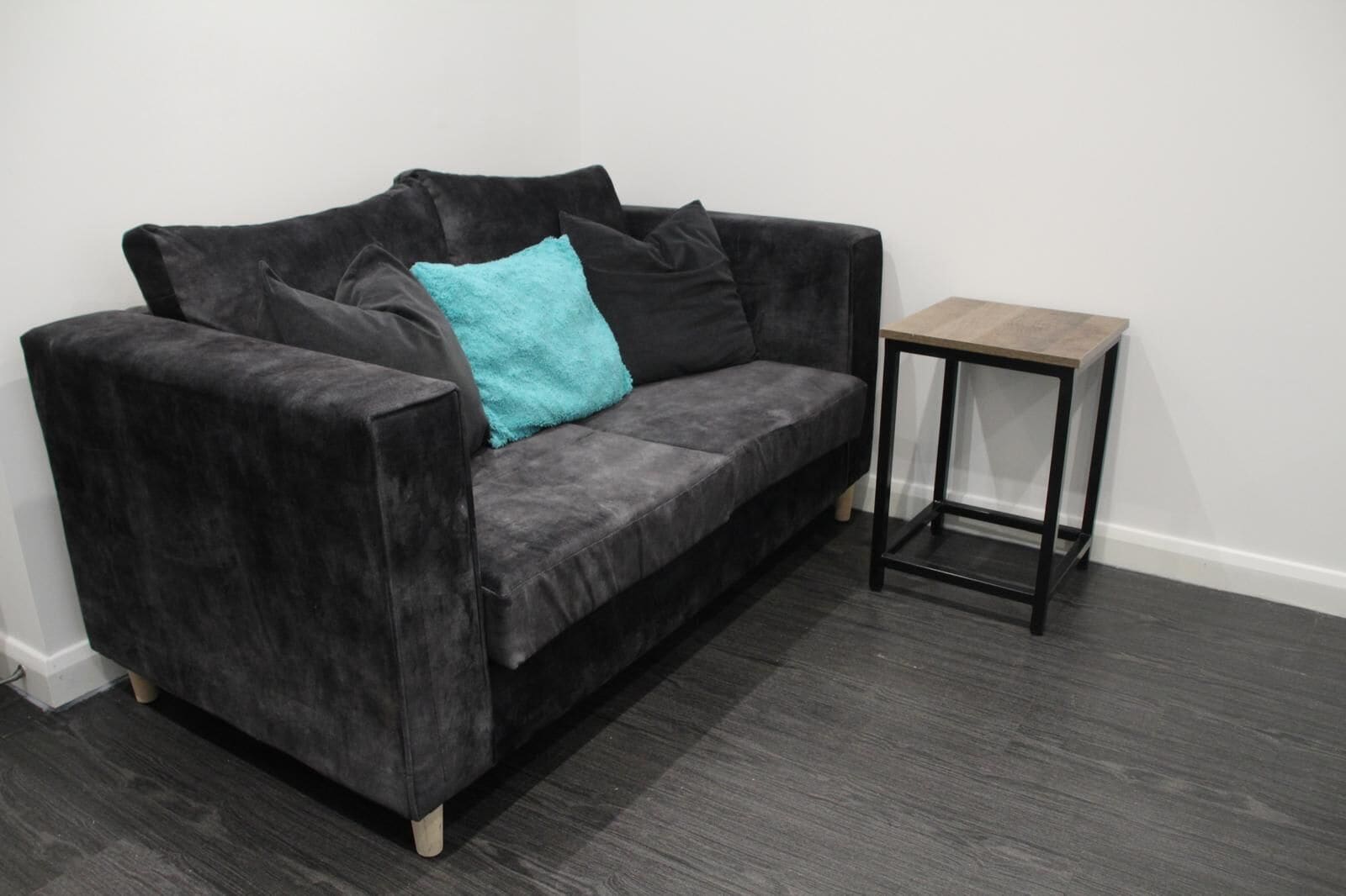 Un canapé gris foncé avec un coussin turquoise et une petite table d’appoint noire.