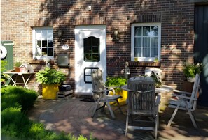 A brick building with a white door, two windows, outdoor seating, and potted plants. - Apartment 'Frieseneck' with Private Garden and Wi-Fi (Zetel)
