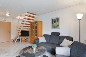 Una sala de estar moderna con un sofá gris, una mesita de centro, un mueble de madera y una escalera que lleva a otro nivel.