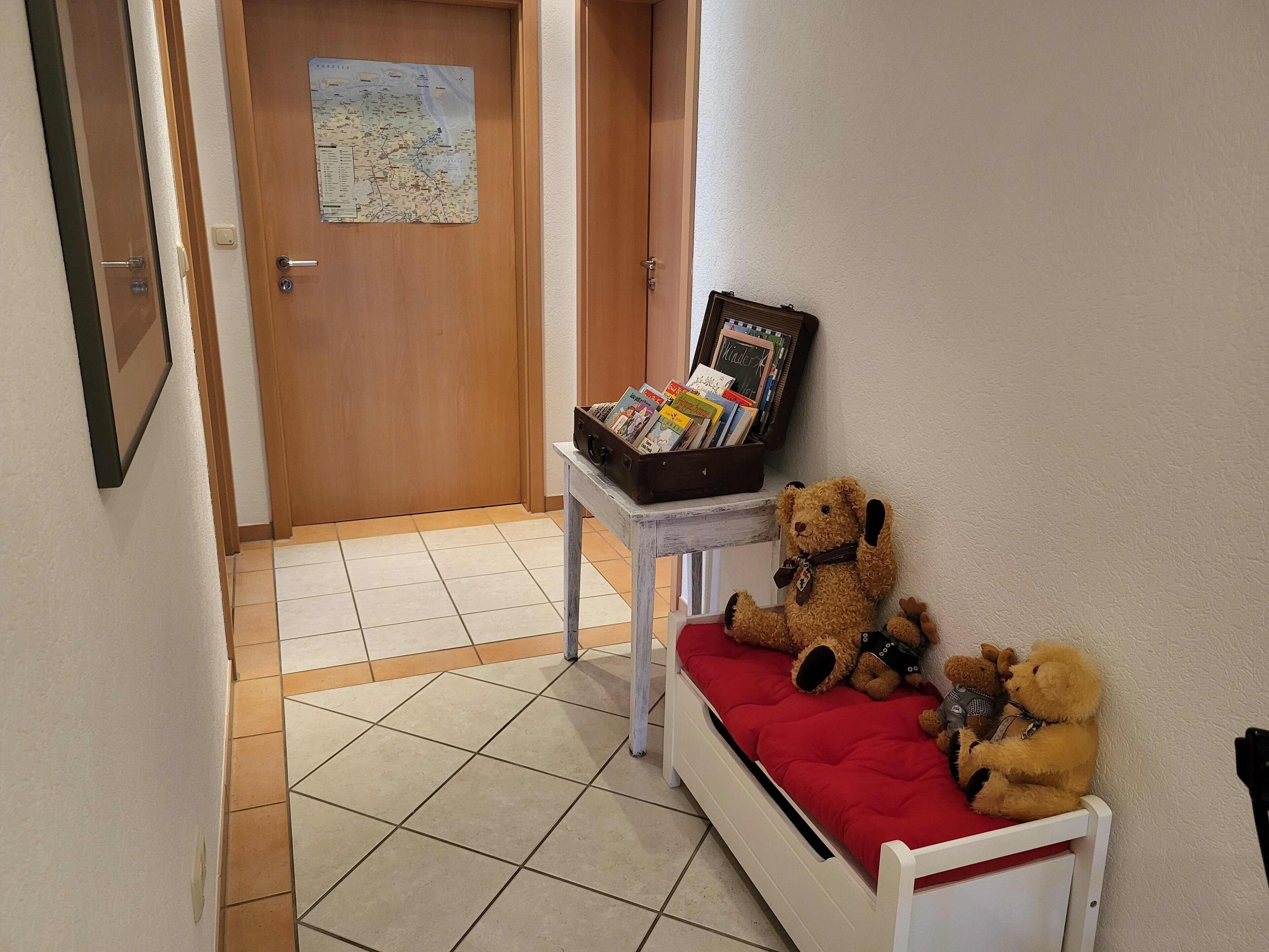 A hallway with a wooden door, a small table with a map, and a bed with a red cushion.