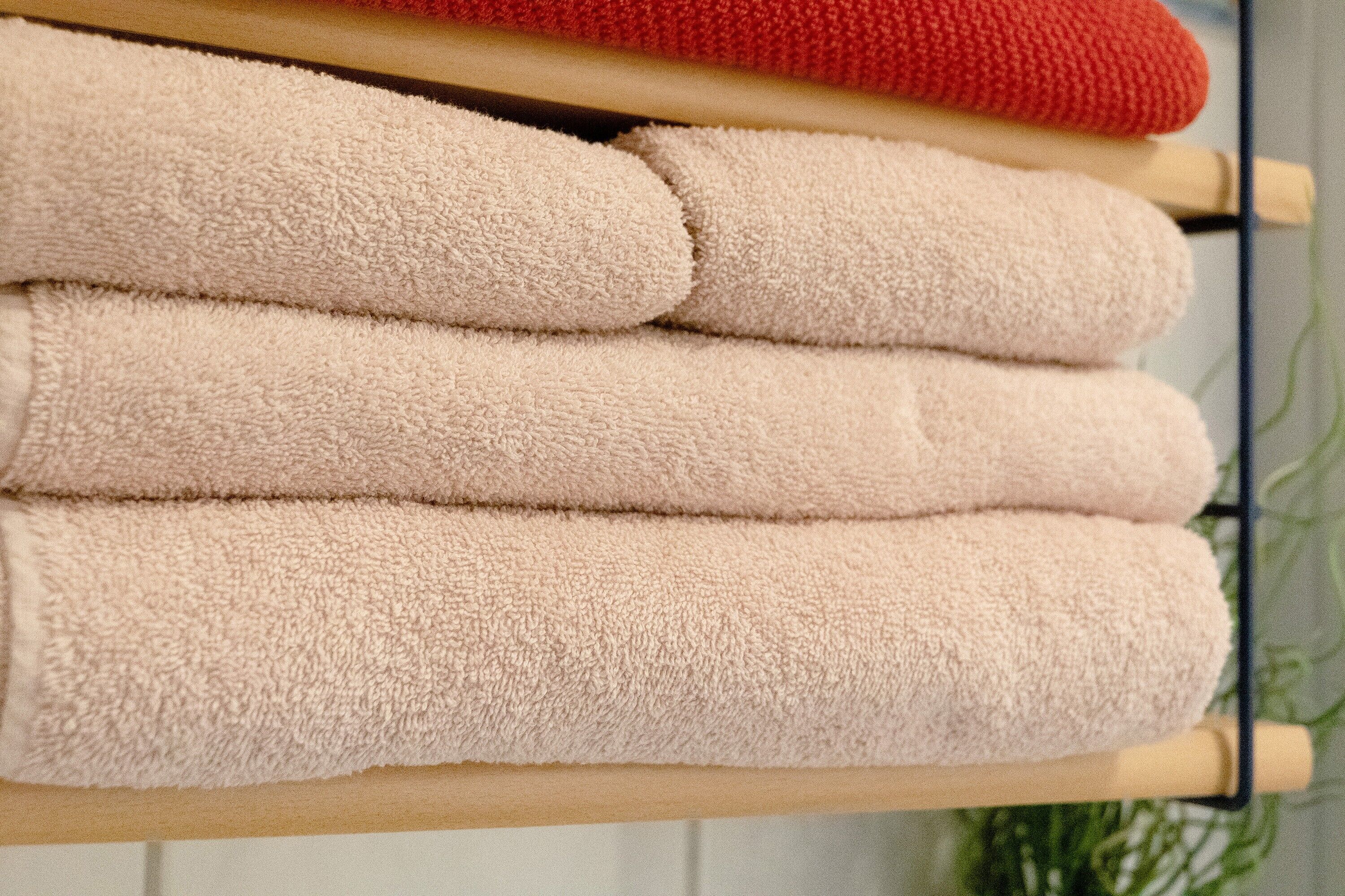 A stack of beige towels on a wooden rack.