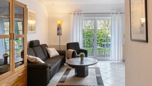 Ein Wohnzimmer mit Sofa, Sessel, Couchtisch und Blick ins Freie durch große Fenster.