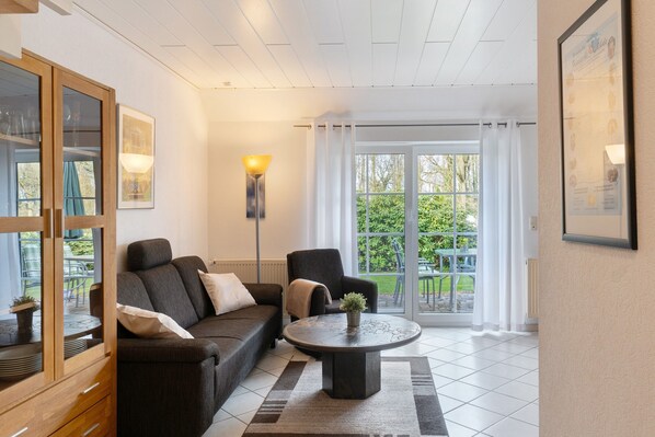 A living room with a sofa, armchair, coffee table, and a view of the outdoors through large windows. - Apartment 'Frieseneck' with Private Garden and Wi-Fi (Zetel)