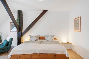 Ein Schlafzimmer mit einem Holzbett, einem grünen Sessel, einem Nachttisch mit Lampe und einer großen Holzbalkenkonstruktion.