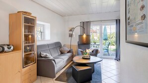 Un salon moderne avec un canapé gris, un meuble en bois, une table basse ronde et une grande fenêtre donnant sur l’extérieur.