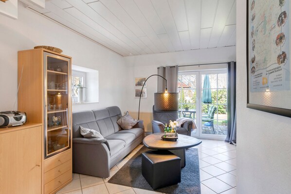 Un salon moderne avec un canapé gris, un meuble en bois, une table basse ronde et une grande fenêtre donnant sur l’extérieur.