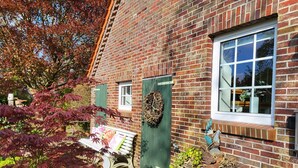 Un bâtiment en briques avec une porte verte, une fenêtre et un banc à l’extérieur.