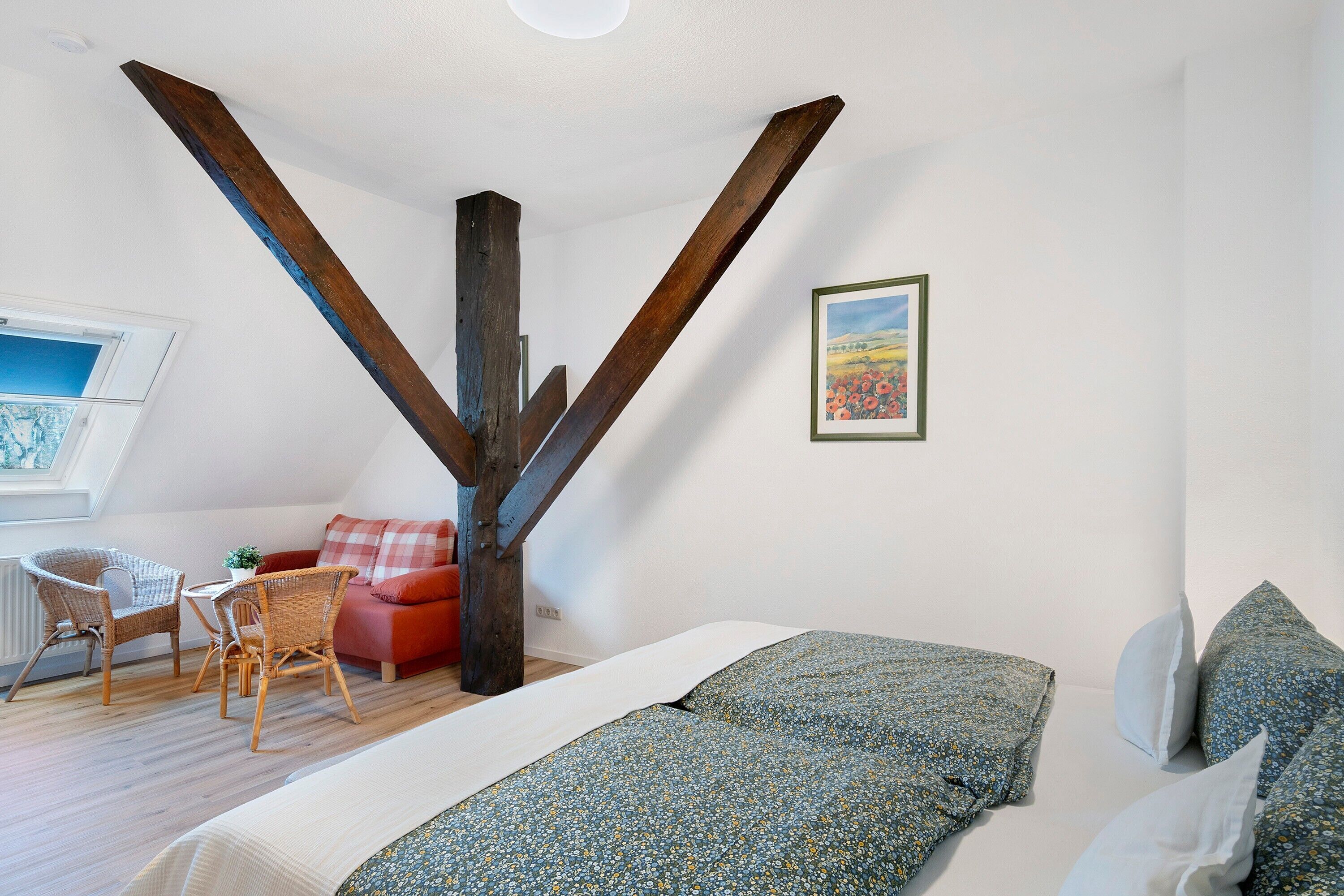 A room with a bed, a chair, a small table, and a painting on the wall.