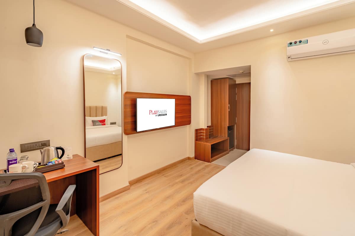 Camera d'albergo con letto, scrivania, sedia, specchio e schermo televisivo che mostra 'PLAYSALS BY DEAN WRIGHT'.