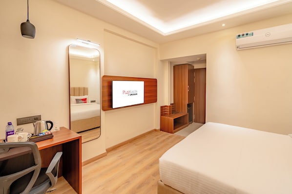 Une chambre d’hôtel équipée d’un lit, d’un bureau, d’une chaise, d’un miroir et d’un écran de télévision diffusant « PLAYSALS BY DEAN WRIGHT ».