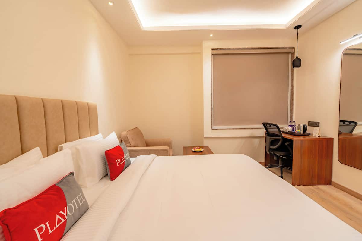 Una camera d'albergo con un letto, una scrivania, una sedia, un tavolino e una finestra con persiane.