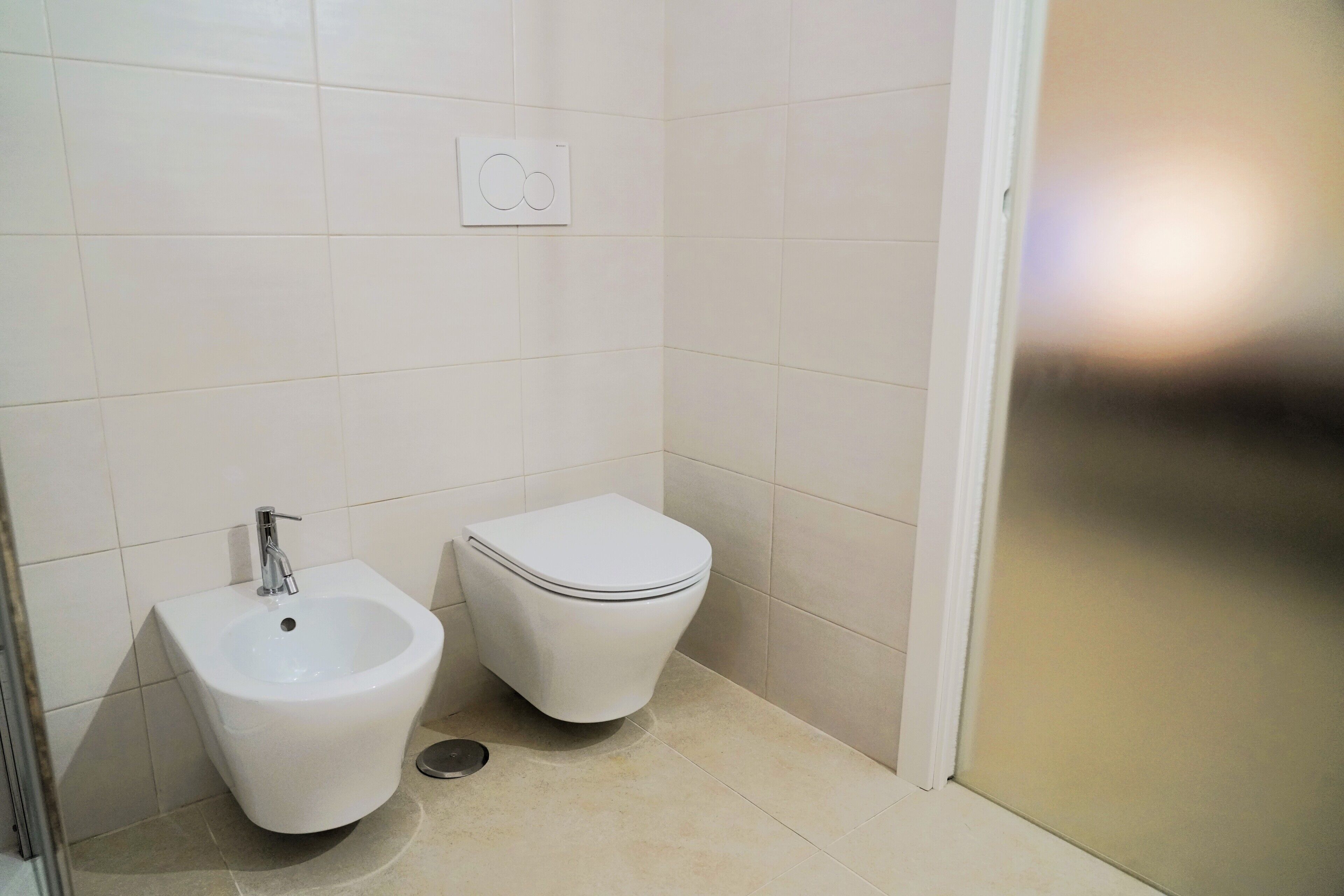 A small, clean bathroom with a bidet, toilet, and a wall-mounted control panel.