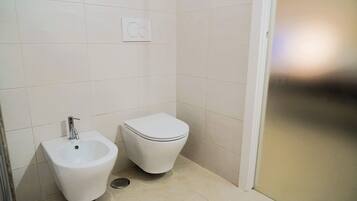 A small, clean bathroom with a bidet, toilet, and a wall-mounted control panel.